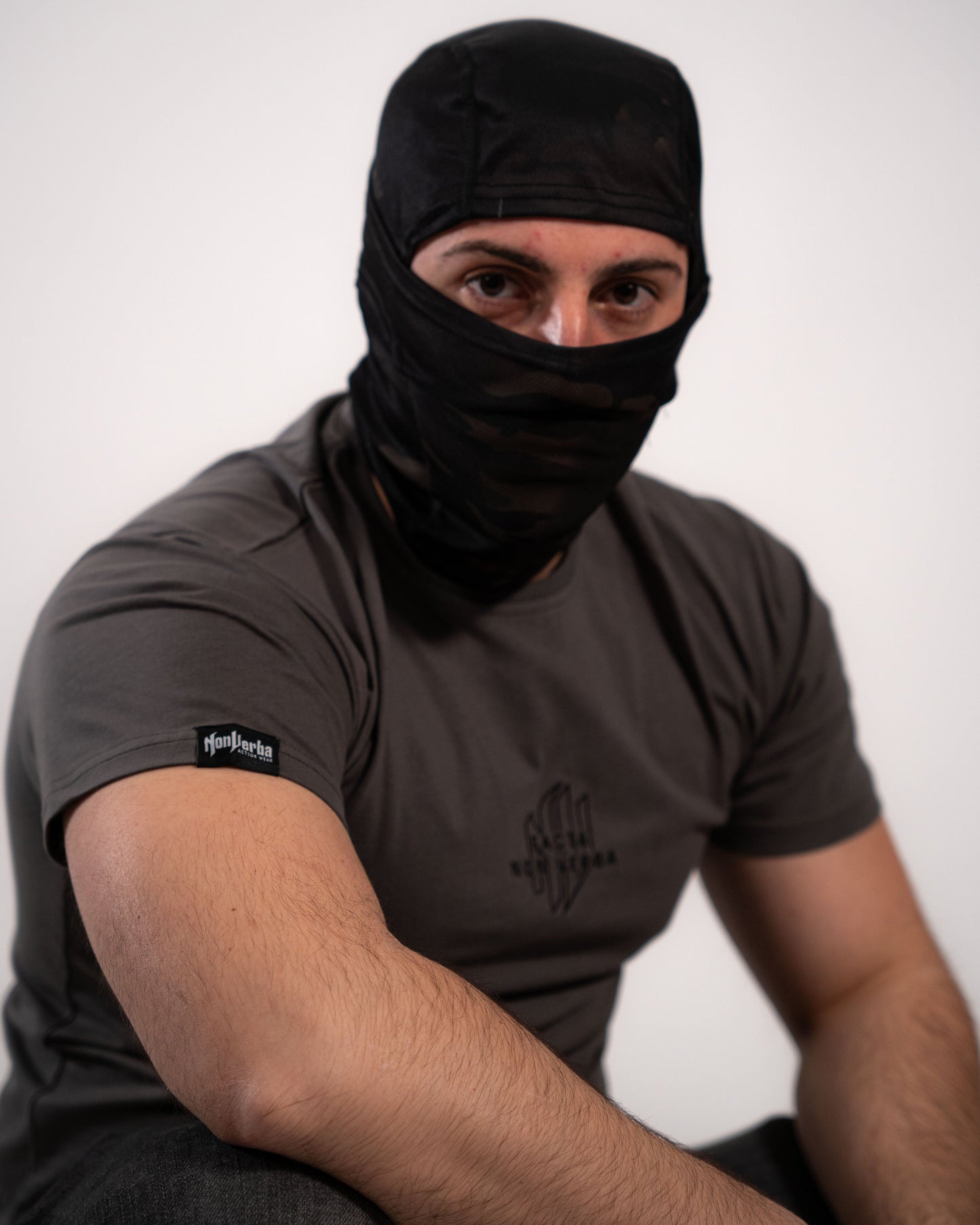 Modelo agachado con un pasamontañas y la camiseta gris de NonVerba puesta.