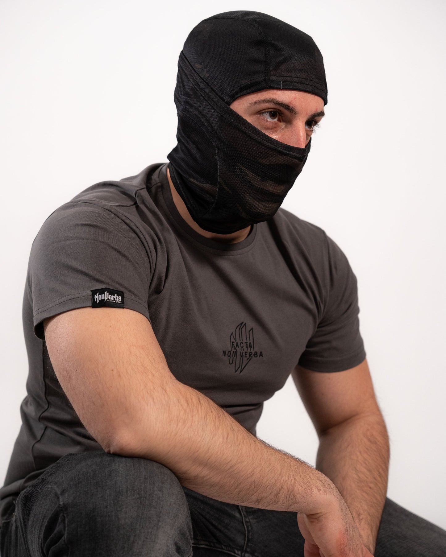 Modelo agachado con la camiseta de NonVerba de colo gris mirando hacia un lado.