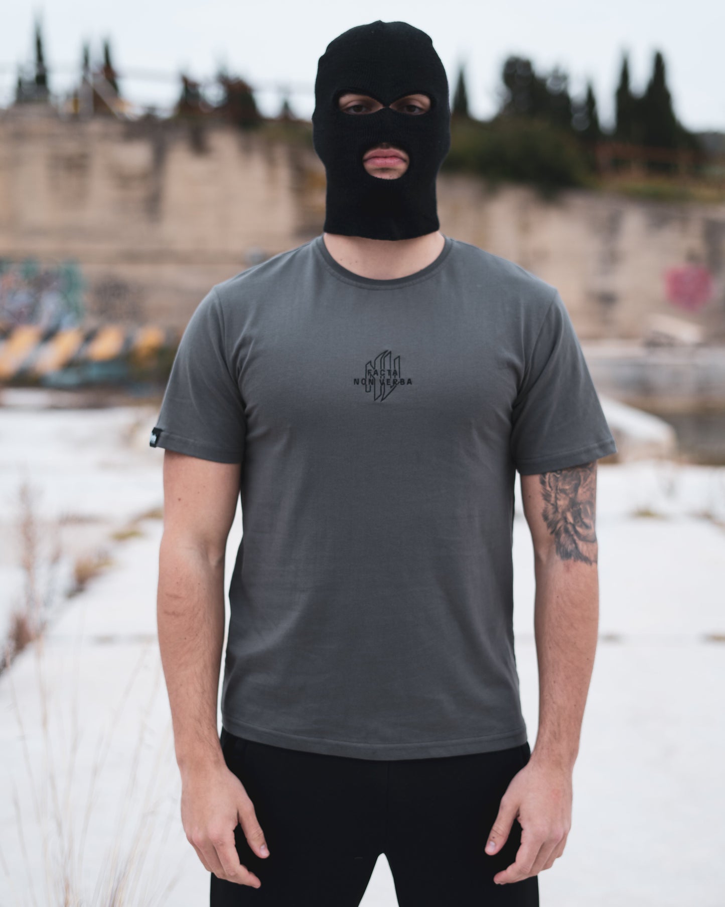 Modelo con la camiseta gris de NonVerba posando de cara en una zona abandonada y con un pasamontañas.