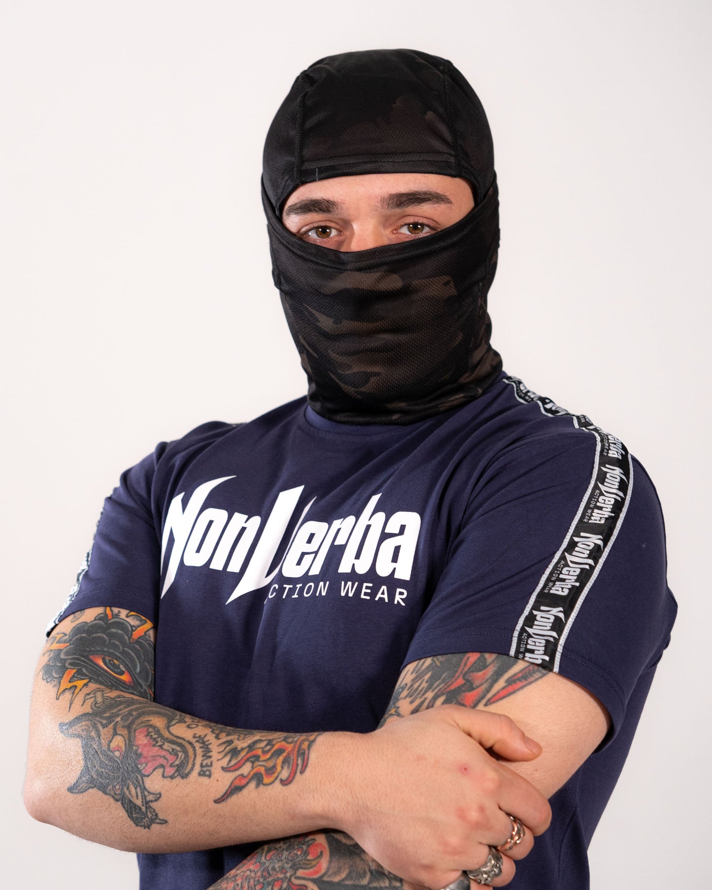 Modelo con la camiseta azul de NonVerba, con un brazo cruzado y un pasamontañas.