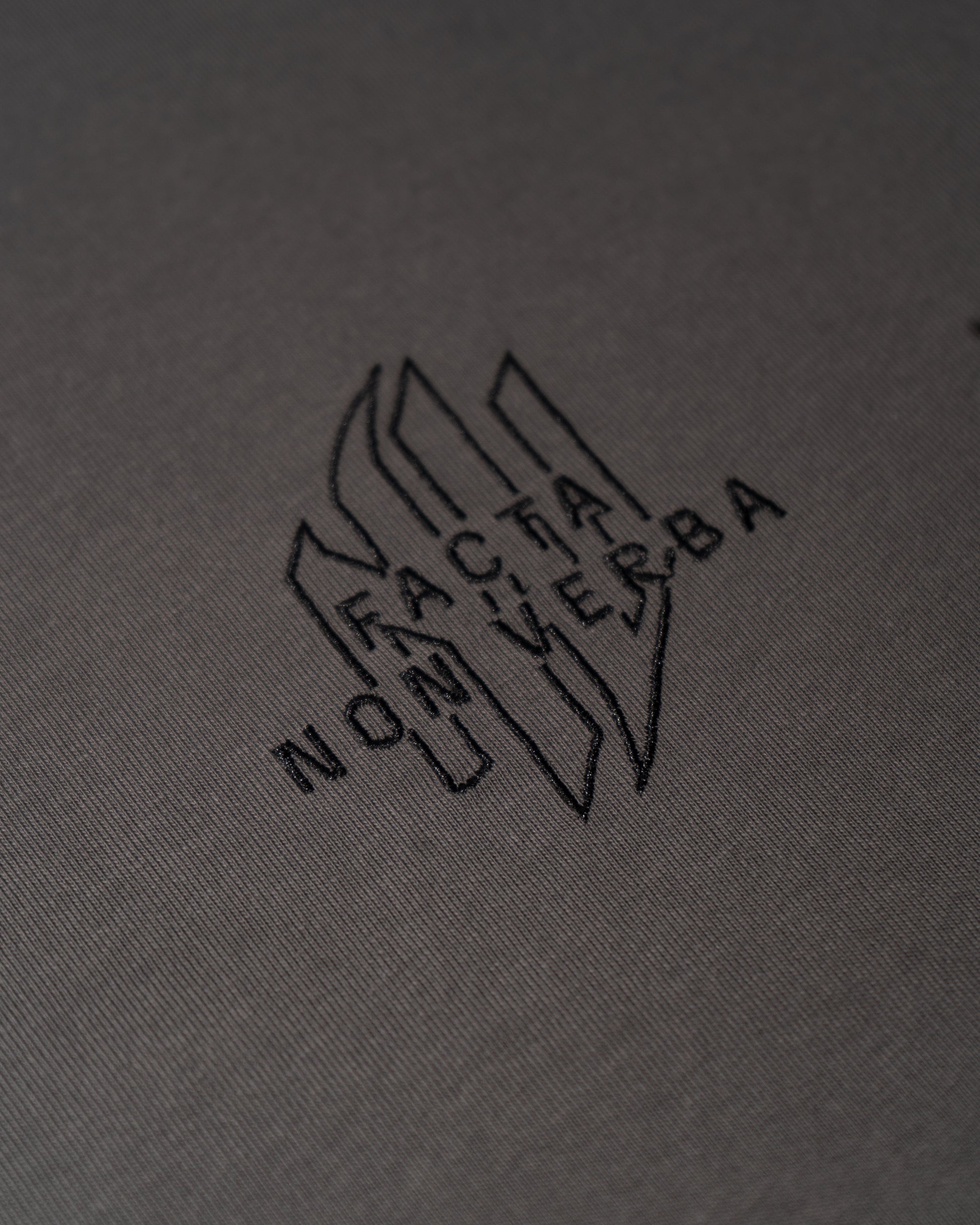 Logotipo de Non Verba bordado sobre el pecho de una camsieta gris.